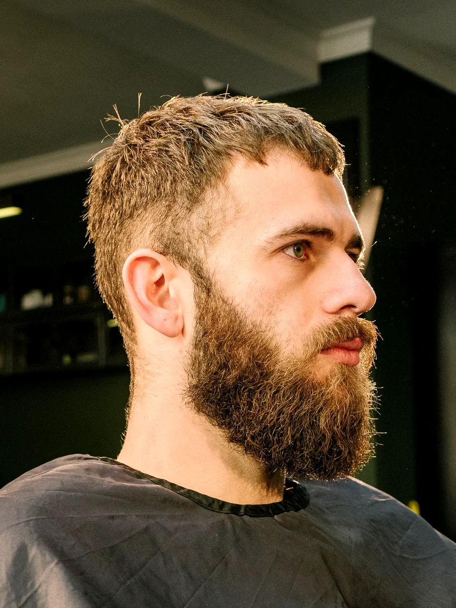 Homme à la barbe taillée, installé dans le fauteuil du salon