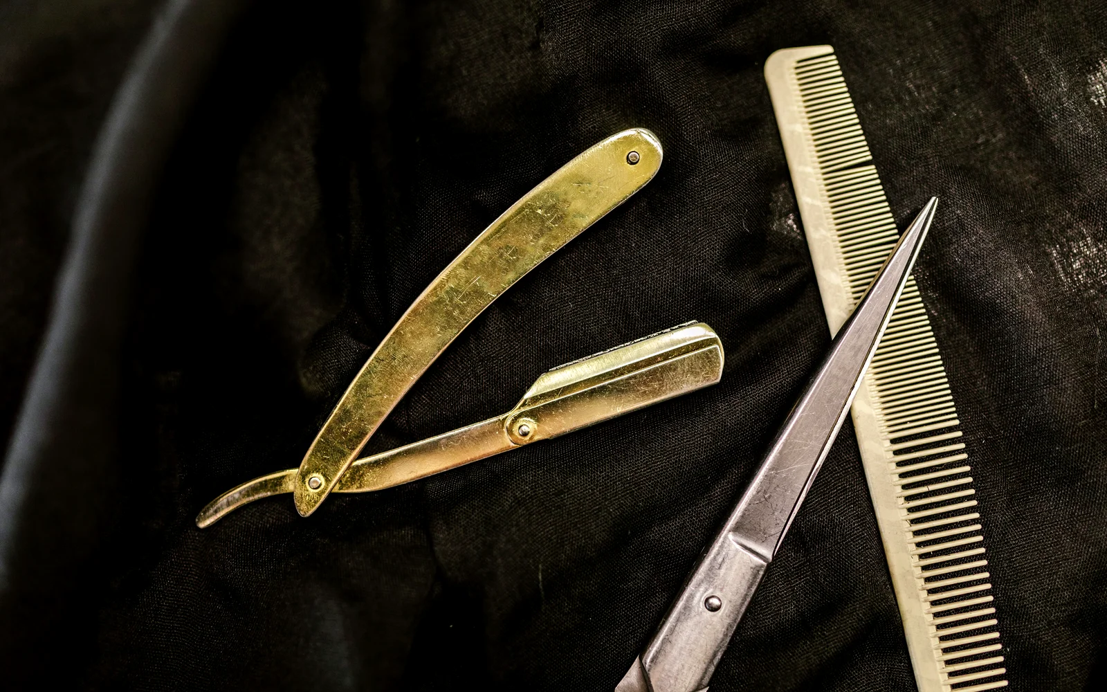 Rasoir droit, peigne et ciseaux de coiffeur posés sur un tissu noir